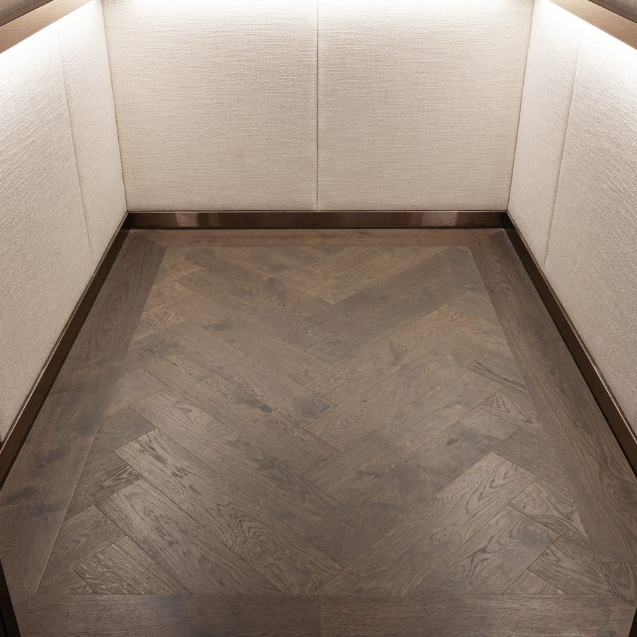 Lift car with the same dark oak herringbone floor carried inside
