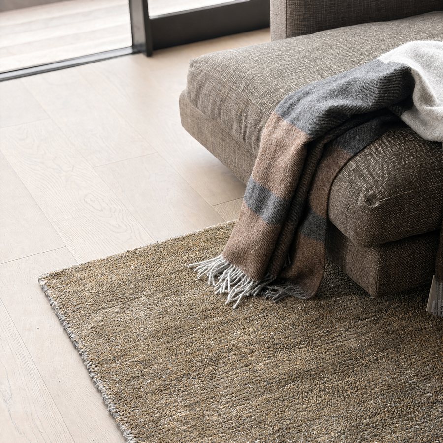 Pale brushed oak floor under a sofa and a woven rug, with a window behind