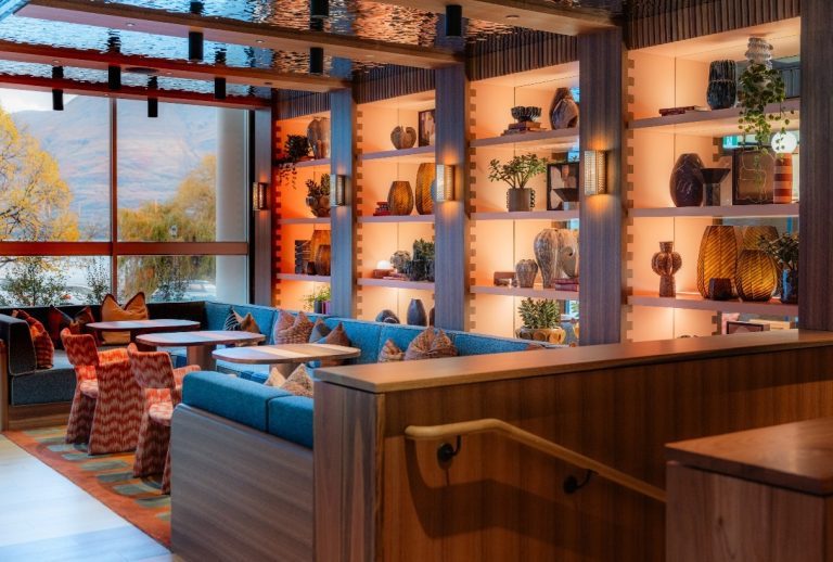 Bar with blue banquette seating, timber joinery and lit shelving, with a lake view