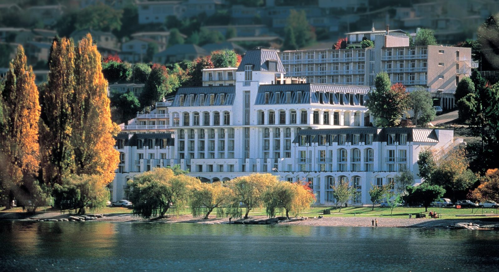 A large white hotel on a lakeshore, framed by autumn poplars and willows