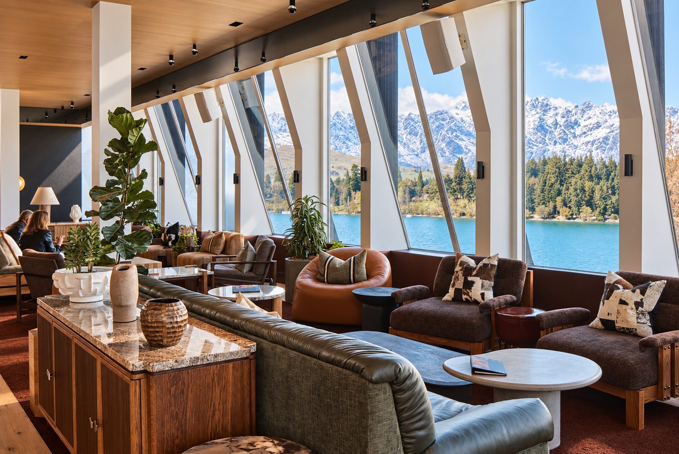 Lounge with timber joinery and tall windows looking across a lake to snow-capped mountains